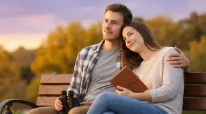 Coppia seduta su una panchina al tramonto con diario zodiacale in mano